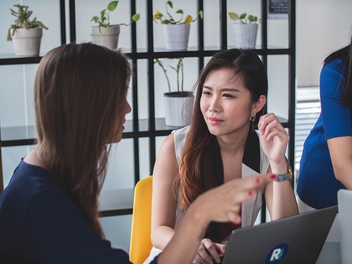 two women sitting on armless chairs near gray laptop computer