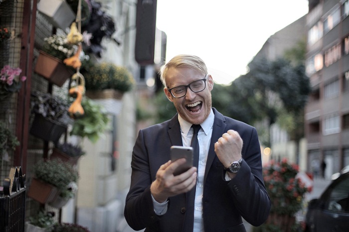 a man in black with a cell phone in hand celebrating a good news message