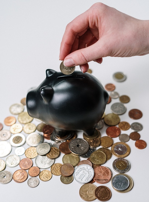 a hand putting coins into a black round box with golden coins around